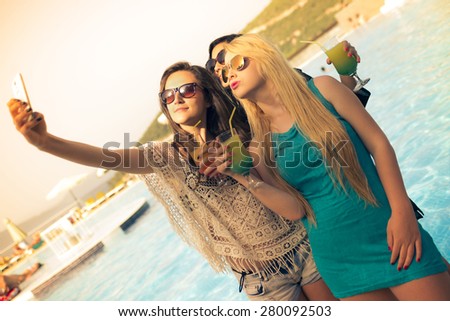 3 young women taking a selfie near the swimming pool in a hotel.