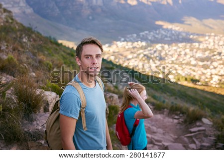 Portrait of a confident young man pausing for a picture while on a hike with a friend on a mountain nature trail 