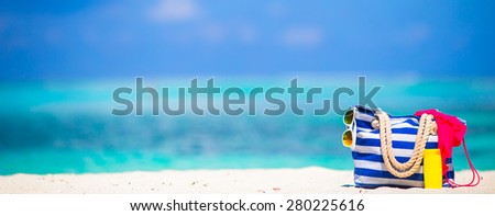 Stripe bag, blue towel, sunglasses, sunscreen bottle and swimsuit on white beach