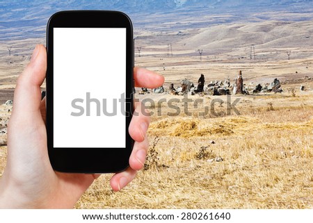 travel concept - tourist photograph view of Zorats Karer (Carahunge) - pre-history megalithic monument in Armenia on smartphone with cut out screen with blank place for advertising logo
