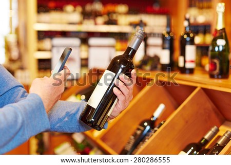 Hand with smartphone scanning wine bottle in supermarket for price comparison