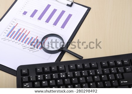 Magnifying Glass With Yearly Graph Bar Representing "Sales/Expenses" with Calculator and Keyboard, Selective Focus 