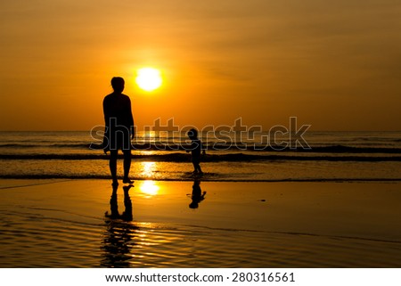 Mother and son silhouettes on beach at sunset