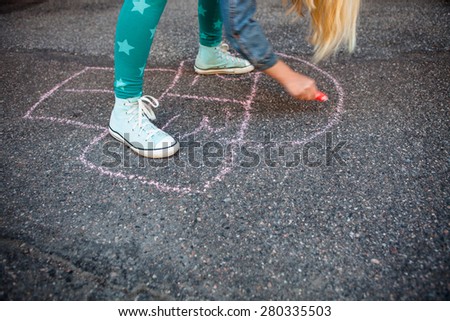 Girl drawing a hopscotch on asphalt with street chalk
