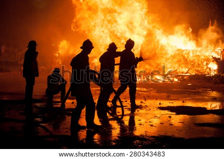 Silhouette of Firemen fighting a raging fire with huge flames of burning timber Royalty-Free Stock Photo #280343483