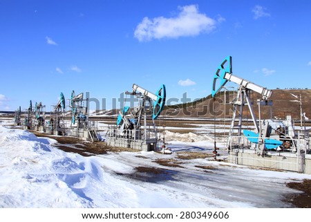 industrial landscape Oil pumps in the field on a background of blue sky and white clouds on a sunny day in early spring