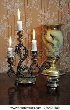 Elegant still life with ornate bronze candelabra and antique goblet on an old wallpaper background