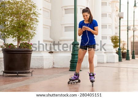 Pretty girl looking for a good song on her smartphone while skating in the city