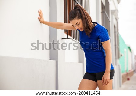 Pretty brunette in sporty outfit taking a break and leaning against a wall to get some air after her workout