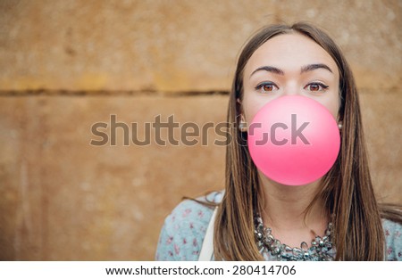 Closeup of beautiful young brunette teenage girl blowing pink bubble gum over a stone wall background Royalty-Free Stock Photo #280414706