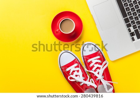 Cup of coffee and laptop computer with gumshoes on yellow background