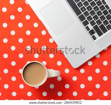 Cup of coffee and laptop computer on red polka dot background