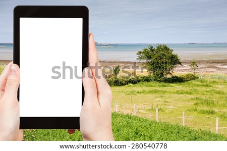 travel concept - tourist photograph green garden on sea coast in Brittany, France on tablet pc with cut out screen with blank place for advertising logo
