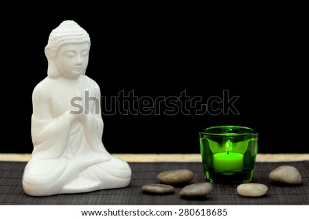 White figure in meditation pose with pebbles and candle in a green glass from point of view