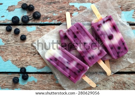 Homemade blueberry vanilla ice pops in a cluster on paper with rustic wood background Royalty-Free Stock Photo #280629056