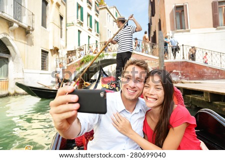 Selfie couple taking picture in gondola on Venice travel vacation. Beautiful lovers on a romantic boat ride across the Venetian canals taking self-portrait pictures with smartphone during holiday.