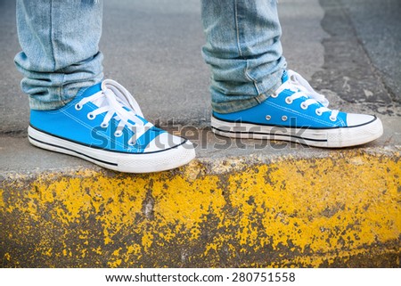 Brand new blue shoes and yellow concrete edge, urban walking theme. Closeup photo with selective focus and shallow DOF