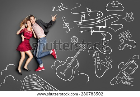 Happy valentines love story concept of a romantic couple sharing headphones and listening to the music against chalk drawings background of musical instruments.