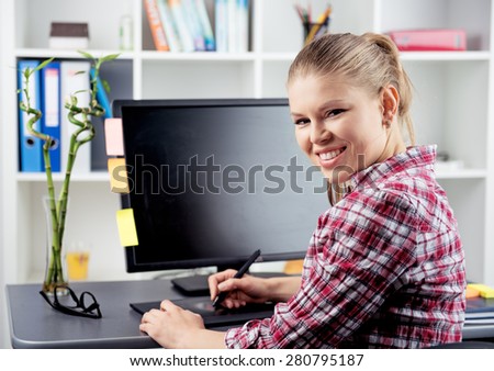 Smiling woman photographer editing photo on digital tablet. Young female retoucher sitting at the desk in the office.