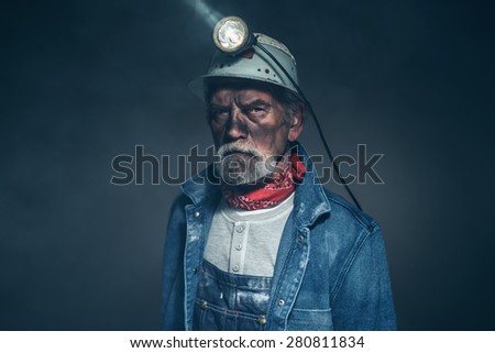 Close up Humorless Bearded Elderly Miner in Denim Jacket and Helmet, Staring at the Camera on a Blurry Background. Royalty-Free Stock Photo #280811834