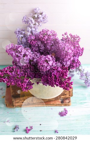 Background  with fresh lilac flowers in bowl  in ray of light on turquoise painted wooden planks against white wall. Selective focus. 