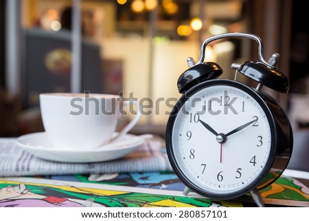 Retro alarm clock with cup of cappuccino and newspaper in coffee shop, coffee break time