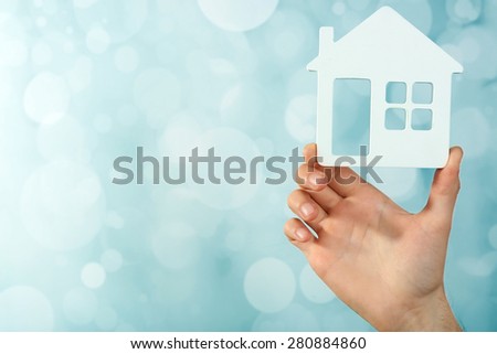 Female hand holding house on light blurred background