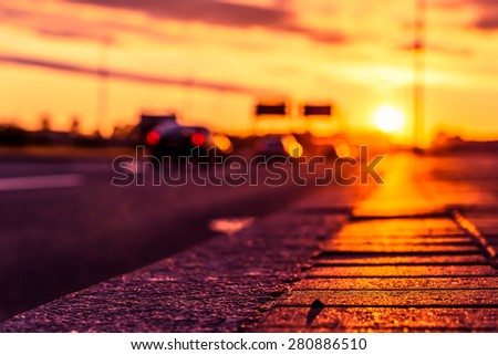 Sunset on the city waterfront. View of the flow of cars from the level of the pavement, image in the orange-purple toning