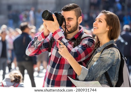 Couple of happy tourists with a map wearing backpacks sightseeing and taking photographs