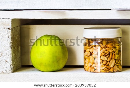Close-up view of green apple and pistachios in a jar on white wooden shelf