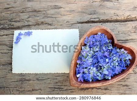 Background with wooden heart with wildflowers and card for message