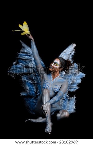 Fairy holding dragonfly on top of stretched hand. Studio, dark background.
