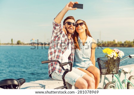 Collecting the bright moments. Smiling young couple making selfie while sitting on parapet near their bicycles 