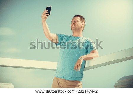 Handsome man tourist on pier taking selfie with smartphone. Fashion guy enjoying summer travel vacation by sea. Relax and technology concept.