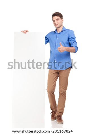 Full body picture of a young fashion man holding a empty board while showing the thumbs up gesture.