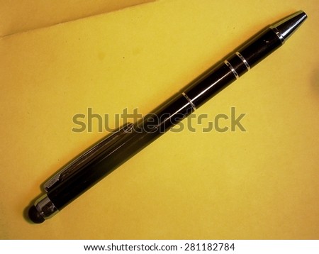 Royalty Free Photograph - Isolated Slender Black Ink Pen with Silver Bands lying on a Brightly Colored Yellow Piece of Paper - with Copy Space
