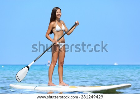 SUP Stand up paddle board woman paddleboarding on Hawaii standing happy on paddleboard on blue water. Young biracial Asian Caucasian female model on Hawaiian beach on summer holidays vacation travel.