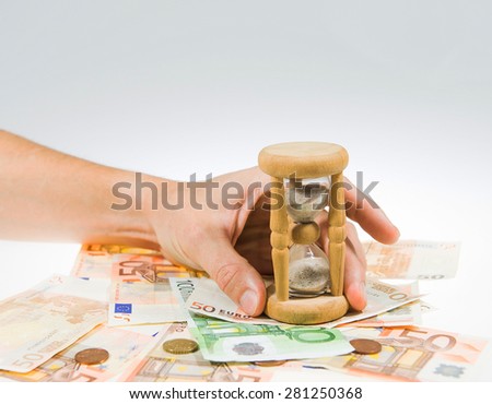 A hand is holding sandglass on top of the euro currency money. Grey and white gradient background