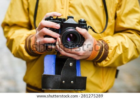 A young guy hipster, holding oldschool film camera, day outdoors, close up, center frame, makes photo