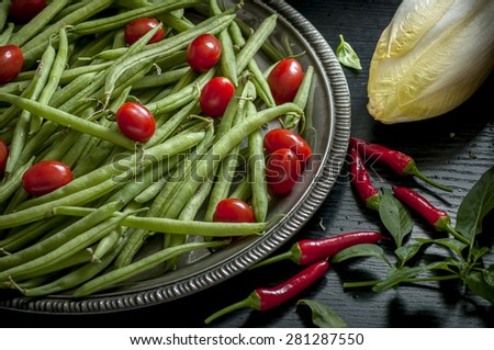 green peas, cherry tomatoes, red chili and chicory on black background