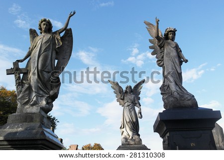 Three angel statues stand tall against the blue sky pointing towards heaven.  Royalty-Free Stock Photo #281310308