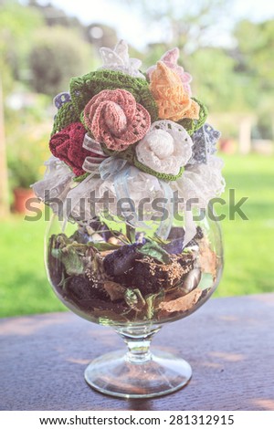 decorative centerpieces and potted flowers made of wool and cotton made crocheted by hand with colored ribbons, on a wooden table with green background garden