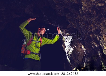 Man walking and exploring dark cave with light headlamp underground. Mysterious deep dark, explorer discovering mystery moody tunnel looking on rock wall inside. Royalty-Free Stock Photo #281367482