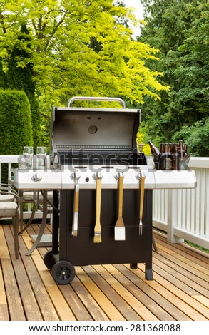 Vertical photo of an open barbecue cooker with cookware and cold beer in bucket on cedar wood patio. Table and colorful trees in background. Royalty-Free Stock Photo #281368088