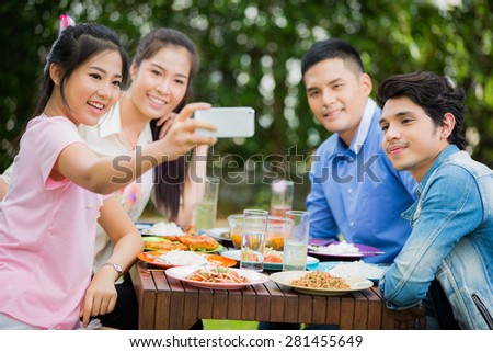 Asians are eating Thailand food garden on the grounds. While eating a woman on the phone taking pictures with friends in a selfie