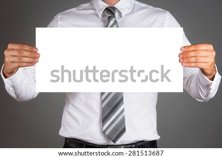 Business man holding a blank white board, isolated on dark gray background.