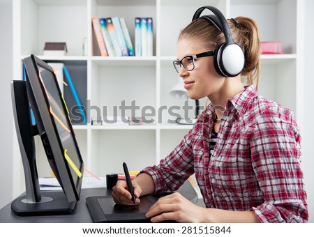 3d animator drawing on graphic tablet listening music in headset. Young positive female designer holding stylus sitting at computer in the office. 