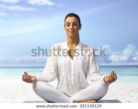 Young woman meditating eyes closed on the beach, smiling.