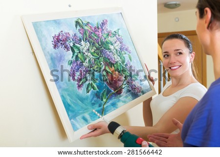 Young man and happy girl hanging art picture in frame