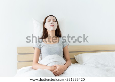 Asian woman lying down and using facial mask at living room